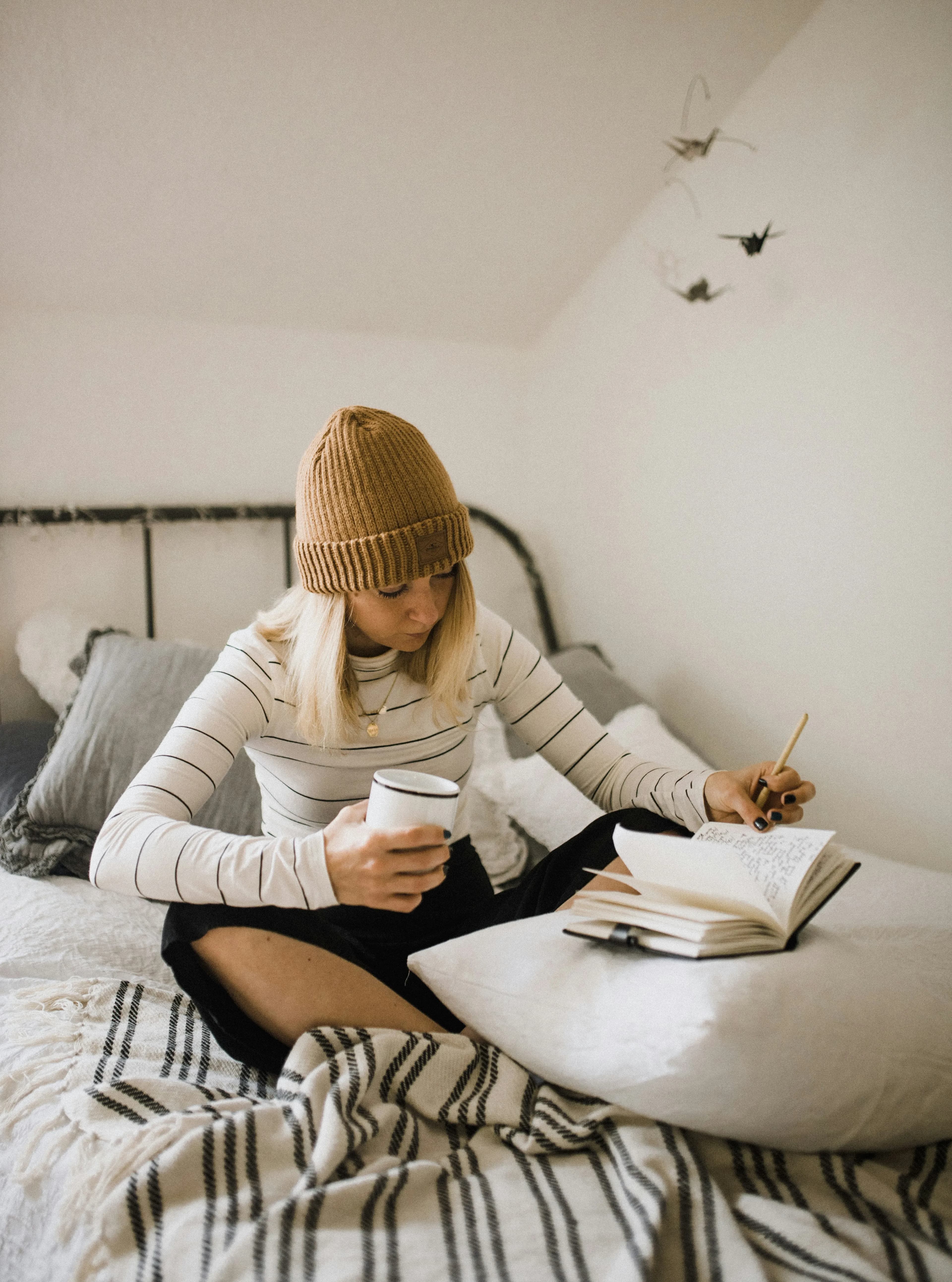 Woman writing in a journal on her bed while holding a mug